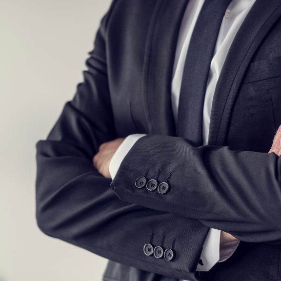 Torso of a businessman standing with folded arms in a classic black suit, toned retro effect.